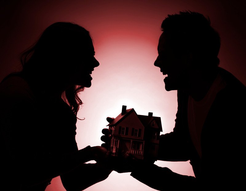 Two people in silhouette facing each other in argument, both gripping a model house between them